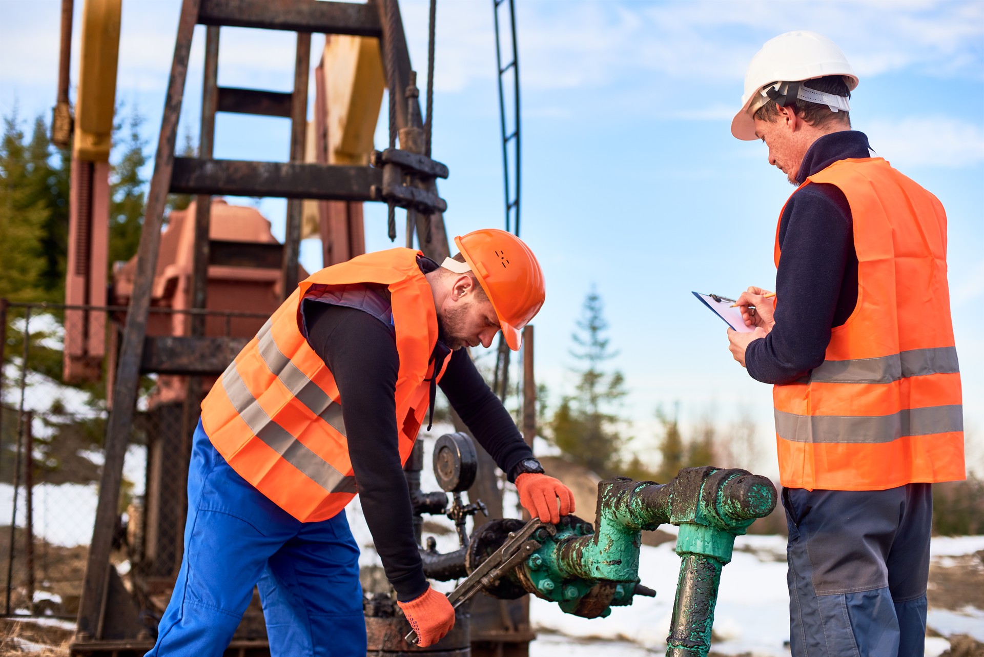 Oil workers in uniforms controlling progress work at local oil pump station on sunny day